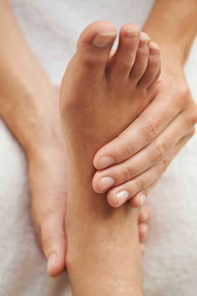 Hænder der giver en afslappende fodmassage, fokuseret på forsiden af foden med blødt fokus baggrund.