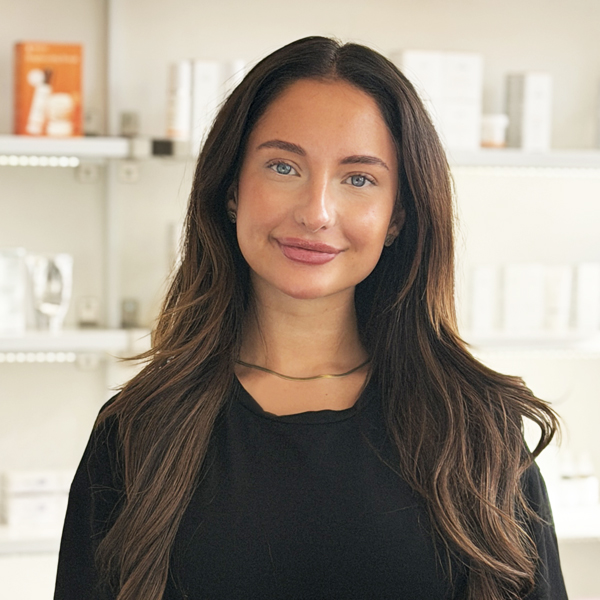 Alisa, medarbejder hos Go Beauty, smilende foran hylder med skønhedsprodukter.
